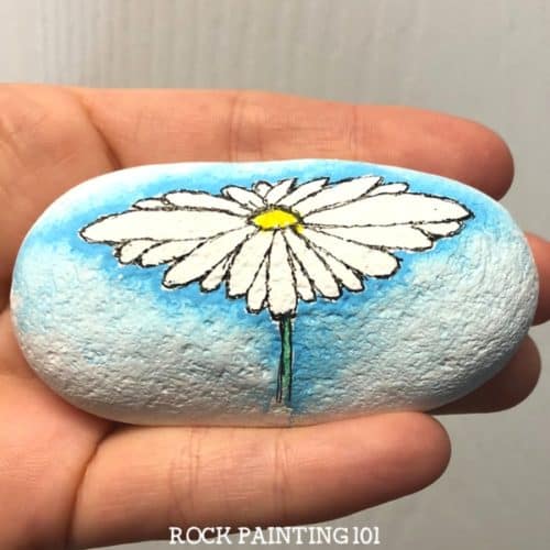 Create a watercolor effect with Posca paint pens or regular acrylic paints. This easy tutorial will walk you through a fun technique by painting a daisy rock. Watch the video and find out how easy this process is. It's perfect for rock painting beginners!