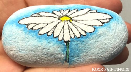 Create a watercolor effect with Posca paint pens or regular acrylic paints. This easy tutorial will walk you through a fun technique by painting a daisy rock. Watch the video and find out how easy this process is. It's perfect for rock painting beginners!
