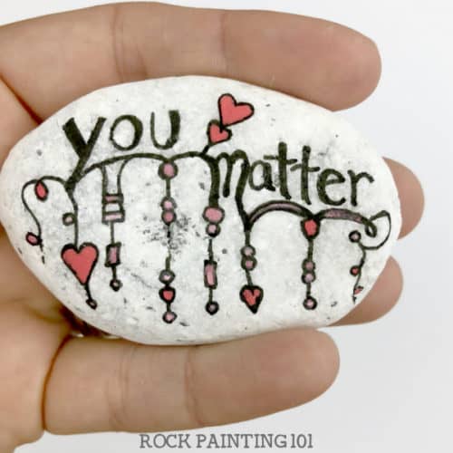 Are you participating in International Drop A Rock Day? Check out all the fun details about this fun day that takes rock hunting to a new level by spreading love and kindness around the world. #internationaldroparockday #droparock #kindnessrocks #youmatter #redheart #howtopaintrocks #zendangle #dangle #rockpainting101