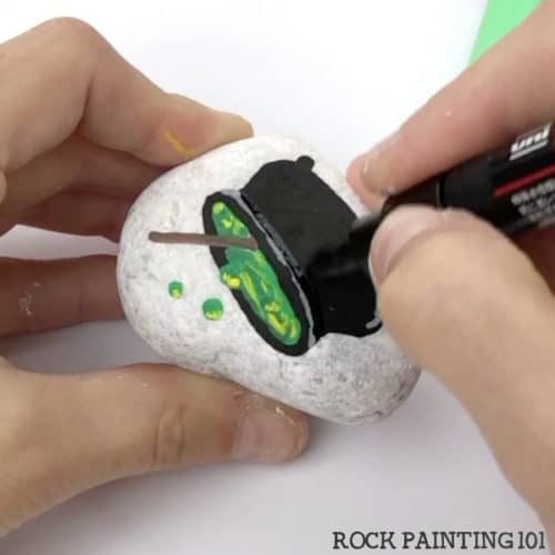 Paint a witch's cauldron with this step by step tutorial. This spooky fun Halloween rock painting idea is perfect for beginners! #witchescauldron #halloweenrocks #paintedrocks #rockpaintingideas #howtopaintbubbles #rockpainting101
