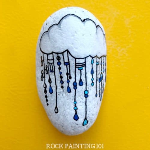 This fun raincloud zendangle painted rock is a great rock painting idea for beginners or for those looking to improve their skill. #zendangle #raincloud #kindnessrocks #rockpainting #paintedrocks #rockart #howtozendangle #dangles #rockpainting101