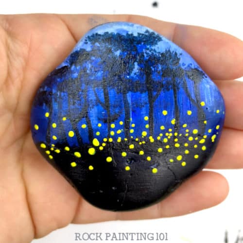 This fireflies rock painting idea is perfect for decorating your night painted rocks. Create layers of trees to make your rock stand out and look amazing. #fireflies #lighteningbugs #night #rockpainting #howtopaintrocks #stonepainting #rockpainting101