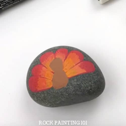 Paint a turkey onto a rock for a fun Thanksgiving rock painting idea. These rocks will look perfect on your Thanksgiving table or hiding around your city! #turkeyrocks #turkeypaintedrock #thanksgivingrock #fallpaintedrocks #howtopaintaturkey #thanksgivingdinnertable #rockpainting101
