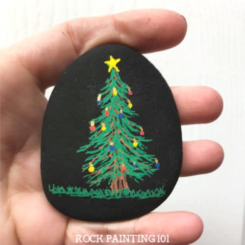 Learn how to paint a Christmas tree for fun holiday rocks. Watch the video tutorial and see just how easy these Christmas stones are to create. They are perfect for stocking stuffers, hiding this winter, or giving to a friend! #christmastree #christmasrockpainting #howtopaintachristmastree #rockpaintingforbeginners #rockart #stonepainting #stockingstuffers #rockpainting101