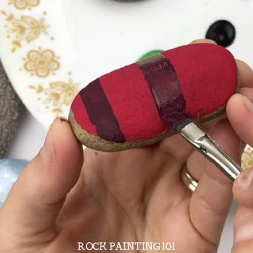 Learn how to paint plaid patterns with these step by step instructions and video tutorial. We used it to paint a fun Christmas rock, but you can use it for any project you have! #plaid #howtopaintplaid #flannel #red #christmasflannel #howtopaintrocks #christmasrockpaintingidea #tutorial #stonepainting #stockingstuffers #holidayrockhunting #giftideas #rockpainting101