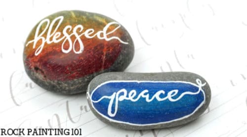 Hand lettering a single word is the best way to learn how to hand letter onto painted rocks. Check out these tips and video tutorial to create kindness rocks or holiday rocks! #handlettering #tips #rockpainting #howtopaintrocks #kindnessrocks #holidayrocks #blessed #peace #paintedrocks #rockpainting101