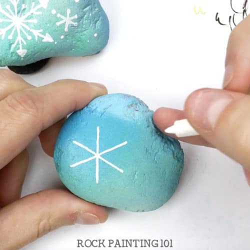 Learn how to draw a snowflake and make beautiful winter painted rocks in one video tutorial! Perfect for winter rock hiding or for decorating your home. #snowflake #rockpainting #howtodrawasnowflake #winter #stonepainting #rockhunting #decor #gifts #rockpainting101