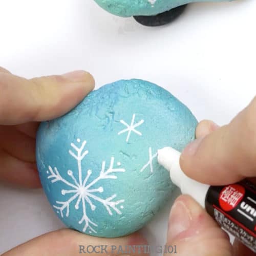 Learn how to draw a snowflake and make beautiful winter painted rocks in one video tutorial! Perfect for winter rock hiding or for decorating your home. #snowflake #rockpainting #howtodrawasnowflake #winter #stonepainting #rockhunting #decor #gifts #rockpainting101