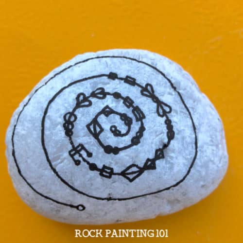 This spiral zendangle rock painting idea is a fun twist on a typical dangle painted rock. Perfect for giving to loved ones or hiding in your city. #spiralzendangle #zendangle #dangles #howtozendangle #rockpaintingideas #love #rockpainting101