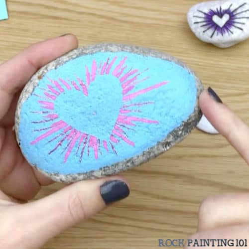 These radial heart painted rocks are perfect for giving to loved ones or hiding around your city! They make amazing kindness rocks! #rockpainting101