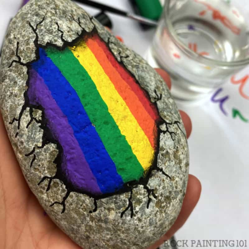 Create this fun optical illusion of a rainbow breaking out of a rock. The video tutorial will walk you through how to paint this easy rainbow rock for beginners. Use this rock painting idea to hide around your neighborhood or give as a gift to loved ones. #rockpainting101 #rainbowrocks